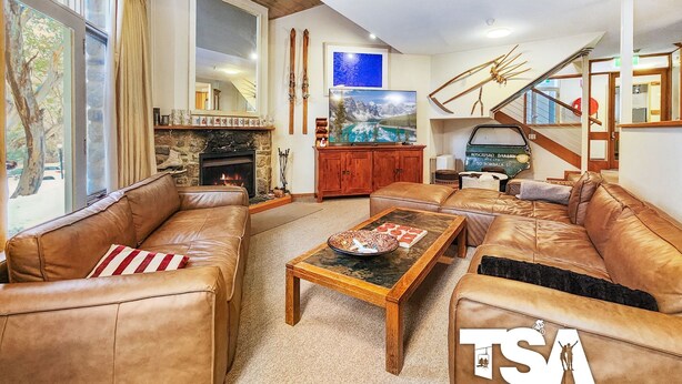 A cozy living room with leather sofas, a fireplace, a television, and skis on the wall.