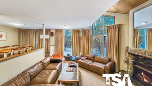 A spacious living room with a fireplace, leather sofas, a dining table, and large windows with curtains.
