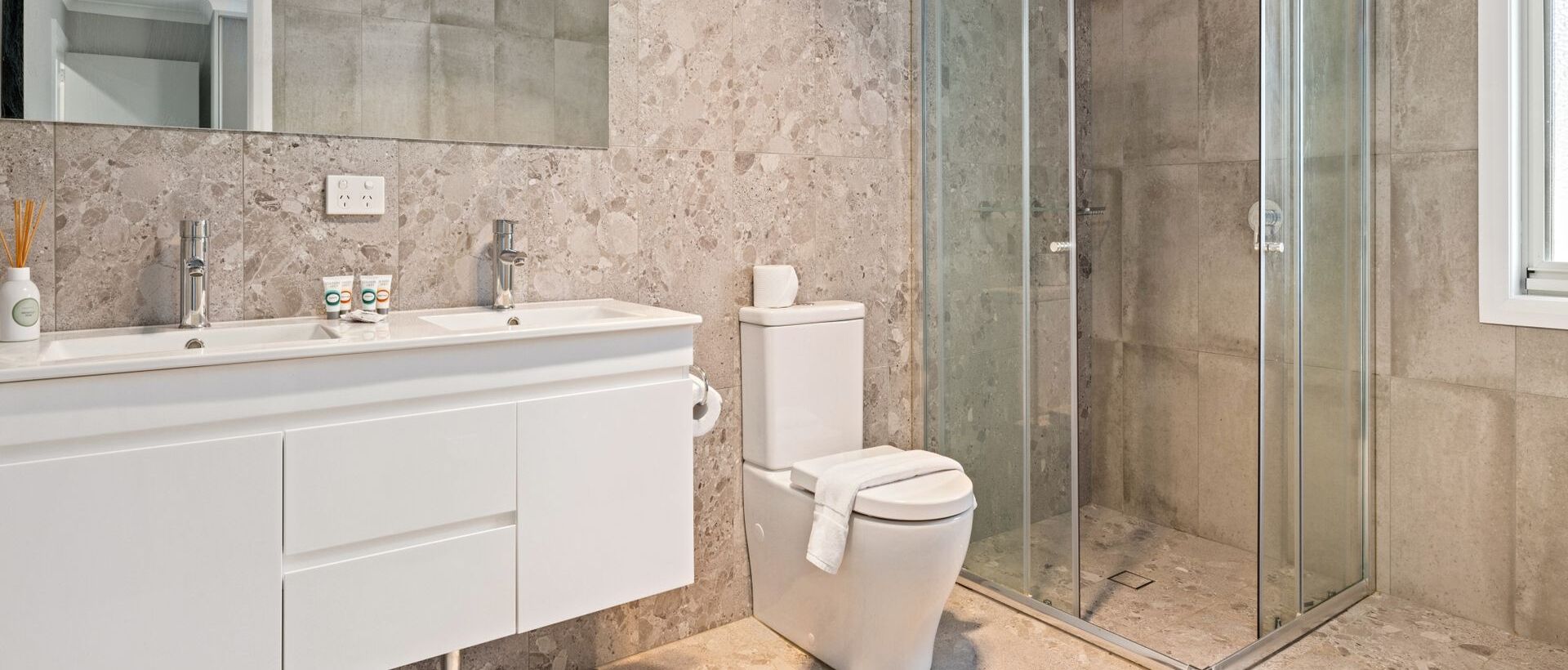 Et moderne badeværelse med vask i marmor, toilet og brusekabine med glasvægge.