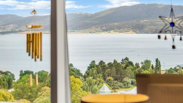 A view from a window overlooking a lake with trees and hills in the distance. - Birralee 1 great lake and mountain views (Jindabyne)