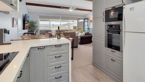 A modern kitchen with grey cabinetry, a built-in oven, and a dining area with a table and chairs. - Birralee 1 great lake and mountain views (Jindabyne)