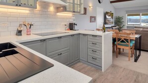A modern kitchen with grey cabinets, a black sink, and a built-in stove. There is a dining area with a wooden table and chairs. - Birralee 1 great lake and mountain views (Jindabyne)