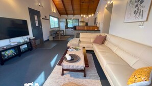 Una sala de estar moderna con un sofá, una mesa de centro y un televisor. Se observa una cocina al fondo con una zona de comedor.