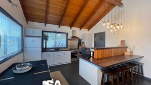 Una cocina moderna con techo de madera, una isla central con taburetes y un ventanal con persianas.