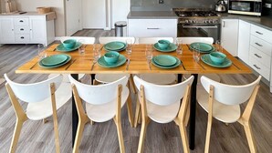 Mesa de comedor con platos azul turquesa y sillas blancas en una cocina moderna con armarios blancos y una estufa de acero inoxidable.