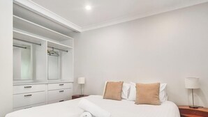 A hotel room with a large mirror, a bed with white linens, two bedside tables with lamps, and a wardrobe with sliding doors. - Mowamba D4 - Central Village (Central Village)