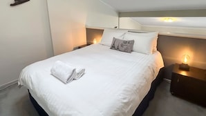 A neatly made bed with a folded towel, white bedding, and a decorative pillow with a design.