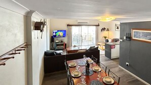 A modern living room with a dining area, a television, and a kitchen in the background.
