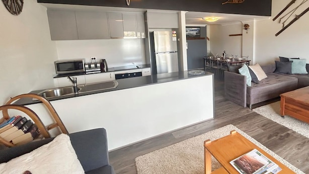 A modern kitchen with a central island, a dining area with a table and chairs, a sofa, and a coffee table.