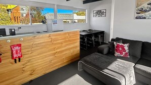 Une cuisine moderne avec des meubles en bois, un plan de travail noir et un coin salon comprenant un canapé et un pouf noirs.