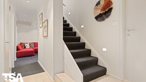 A staircase with carpeted steps leading to a landing. A red sofa with patterned cushions is visible in the background.