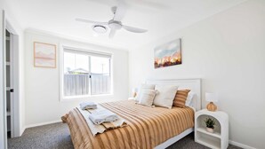 Een slaapkamer met een bed, een plafondventilator, een raam en een schilderij aan de muur.