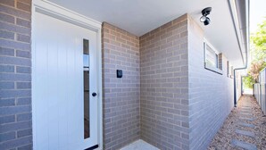 A narrow corridor with a white door, brick walls, and a security camera. - Cozy Getaway - Modern Central Unit | Garden View (Dubbo)