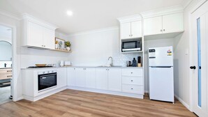 A modern kitchen with white cabinetry, a microwave, a refrigerator, and a wooden floor. - Cozy Getaway - Modern Central Unit | Garden View (Dubbo)