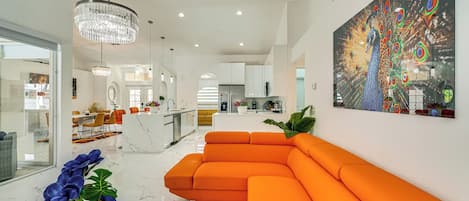 A modern living room with a large orange sectional sofa, a chandelier, and a vibrant peacock painting on the wall.