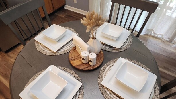 A round dining table with square white plates, two salt shakers, and a decorative vase with dried flowers. - Senseney Cottage~Pet Welcome, Fenced Yard (Clarksville)