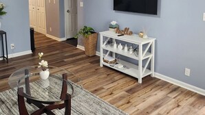 A living room with a TV mounted on the wall, a white console table, and a round glass table with chairs. - Senseney Cottage~Pet Welcome, Fenced Yard (Clarksville)
