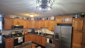 A modern kitchen with wooden cabinets, stainless steel appliances, and a dining area set for four. - Senseney Cottage~Pet Welcome, Fenced Yard (Clarksville)