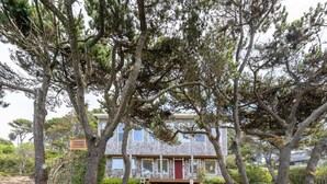 Un bâtiment à deux étages avec une porte rouge, entouré d’arbres adultes et d’un jardin bien entretenu.