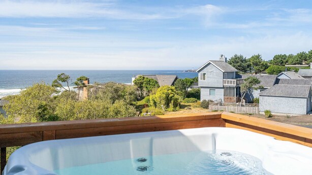 Un jacuzzi sur une terrasse, avec vue sur l’océan et des maisons en arrière-plan.