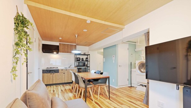 Un espacio habitable moderno con piso de madera, un sofá, una mesa de comedor con sillas, una zona de cocina con electrodomésticos y un televisor.