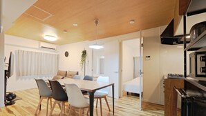Una habitación de hotel moderna con suelo de madera, un área de comedor con mesa y sillas, una kitchenette y un ventanal con cortinas.