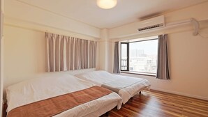 Habitación de hotel con dos camas, un ventanal con cortinas, un equipo de aire acondicionado y suelo de madera.
