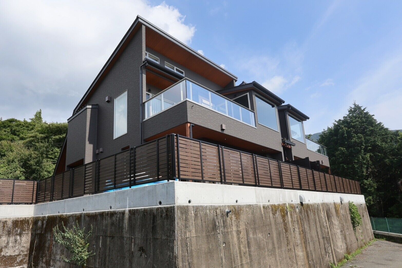 Una casa moderna de dos pisos con balcón, ventanas grandes y cimientos de concreto.