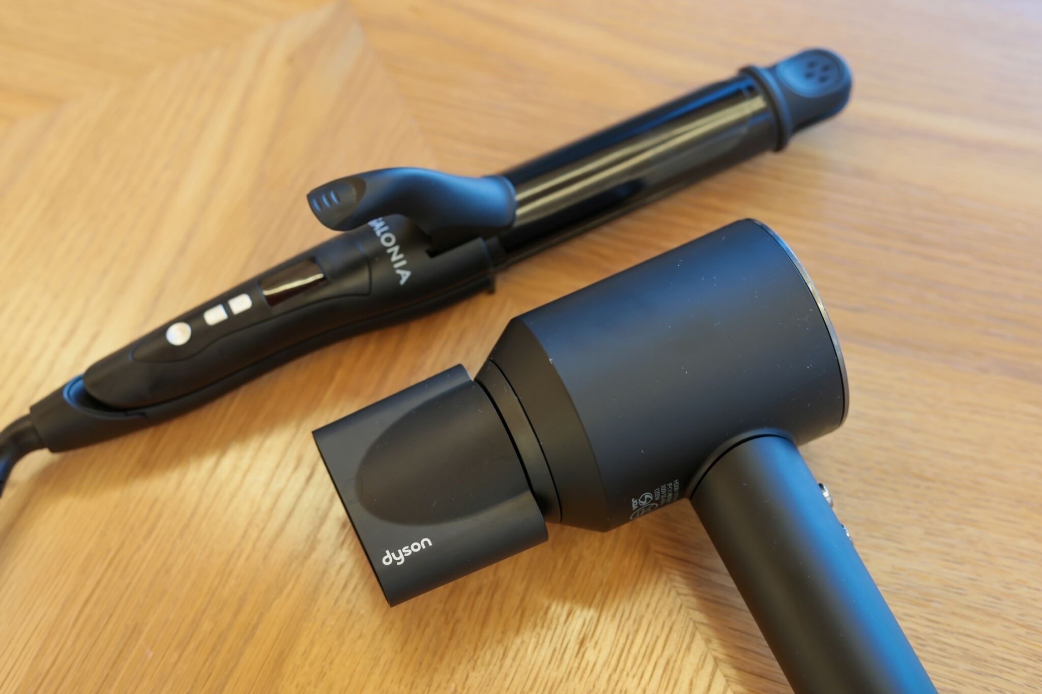 Una herramienta de peluquería negra con cable y un accesorio cilíndrico sobre una superficie de madera.