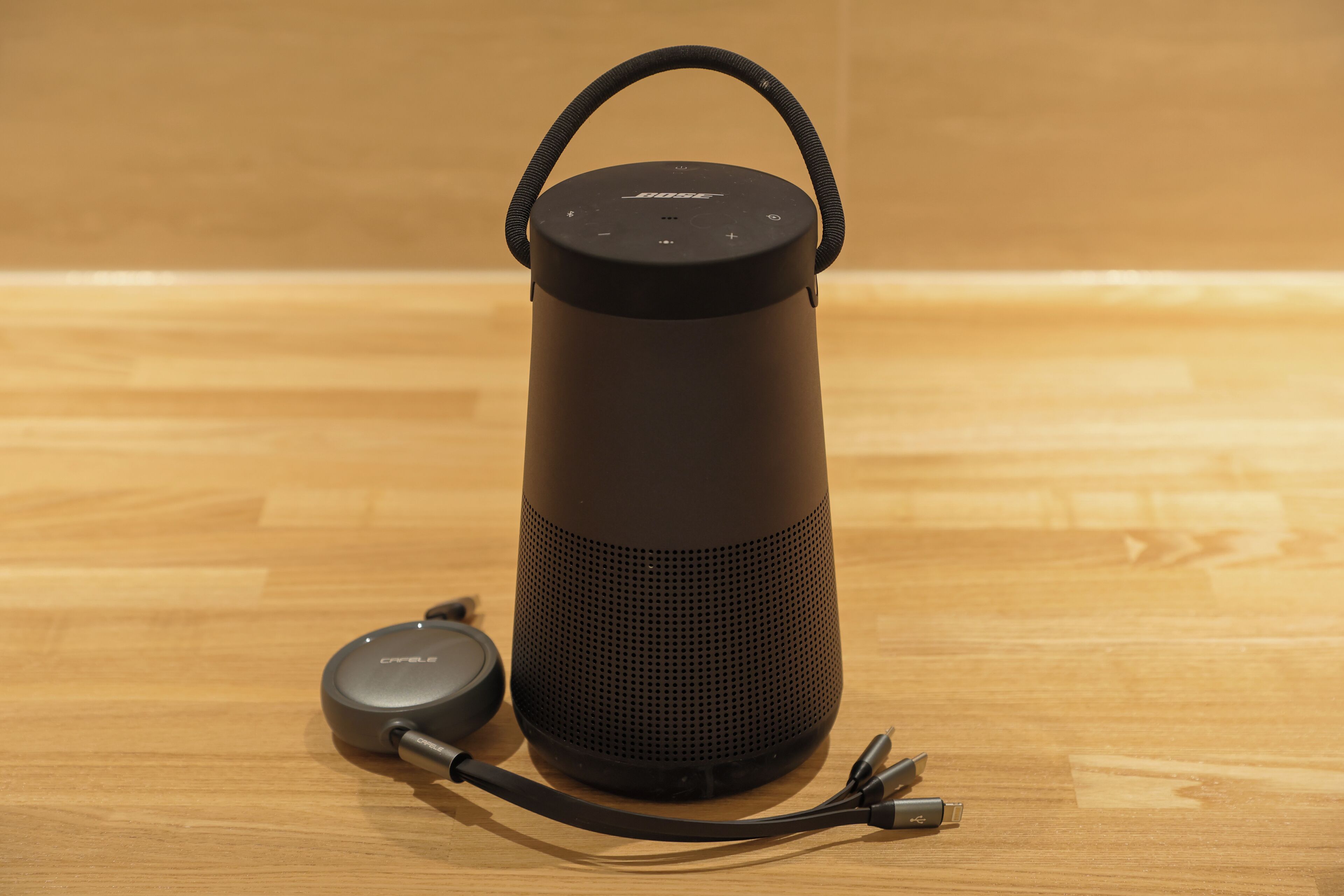 A black portable speaker with a handle on top and a charging cable connected to it.