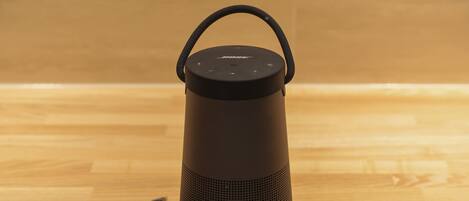 A black portable speaker with a handle on top and a charging cable connected to it.