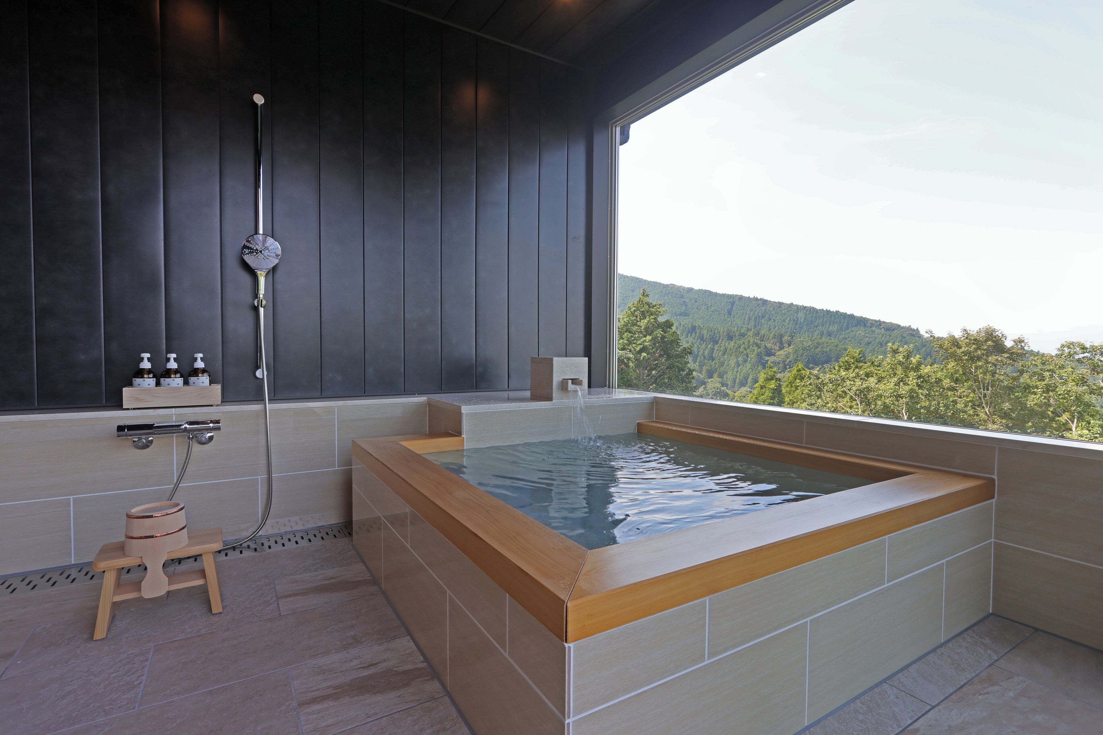 A modern bathroom with a large bathtub, a shower, and a small wooden stool.