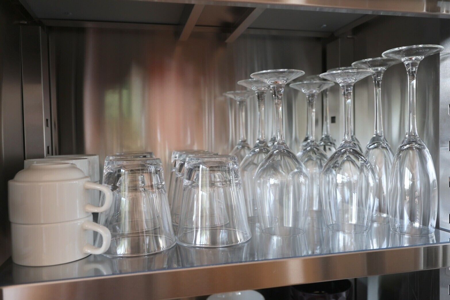 A stainless steel shelf with various glassware, including wine glasses and tumblers, and a white mug.