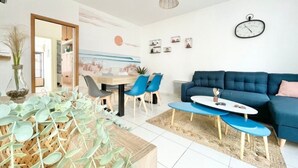 A modern living room with a blue sofa, a coffee table, and a dining area with chairs and a table. - Le Benodet Centre. In the center of town 200m from the beach (Bénodet)