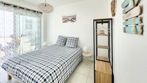 A bedroom with a bed, a hanging light fixture, a wall-mounted shelf, and a window with curtains. - Le Benodet Centre. In the center of town 200m from the beach (Bénodet)