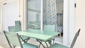 A patio with a table and chairs, a sliding glass door, and a bed visible through the door. - Le Benodet Centre. In the center of town 200m from the beach (Bénodet)