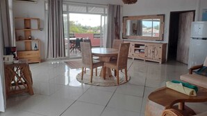 Een ruime woonkamer met een eettafel, stoelen, een bank, een televisie en een groot raam met uitzicht.
