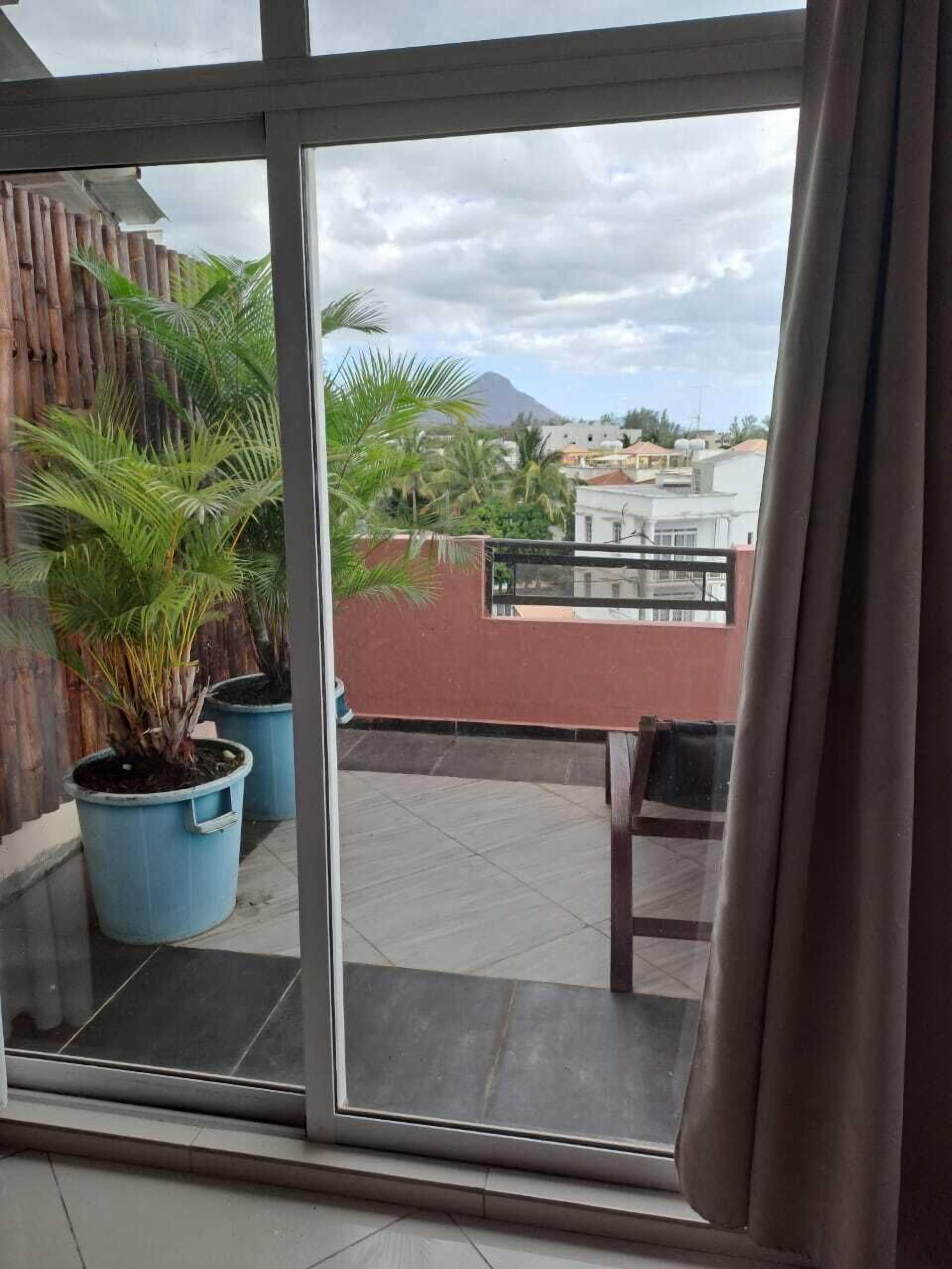 Un balcón con macetas, vista a una montaña y un paisaje urbano distante.