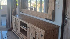 Een houten kast met een grote spiegel erboven, geplaatst in een kamer met een schuifdeur van glas die naar een buitenruimte leidt.