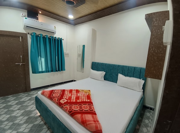 A bedroom with a bed, teal curtains, a wall-mounted air conditioner, a mirror, and a door. - Hotel Shree Balaji (Ujjain)