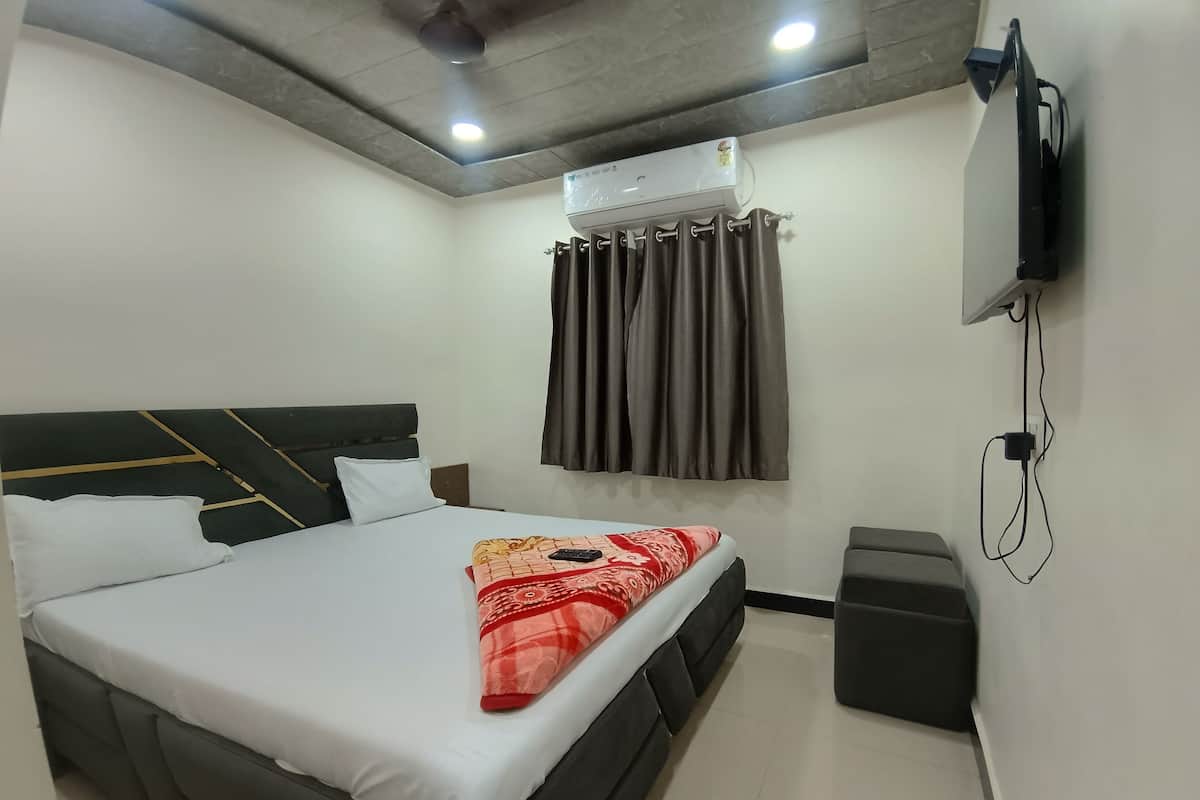 A hotel room with a bed, an air conditioning unit, a television, and a small trash bin.