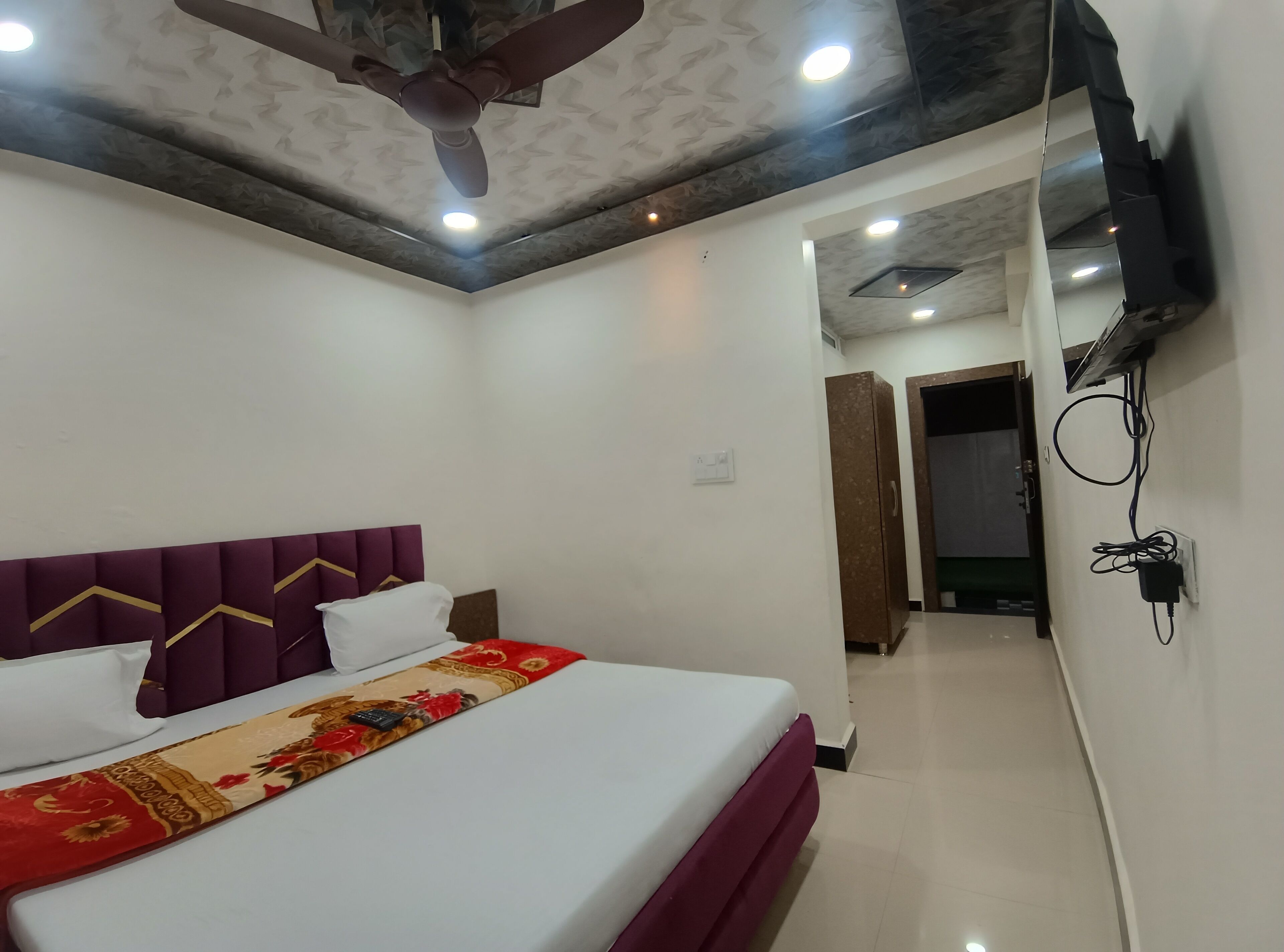 A hotel room with a bed, a ceiling fan, and a hallway leading to another room.