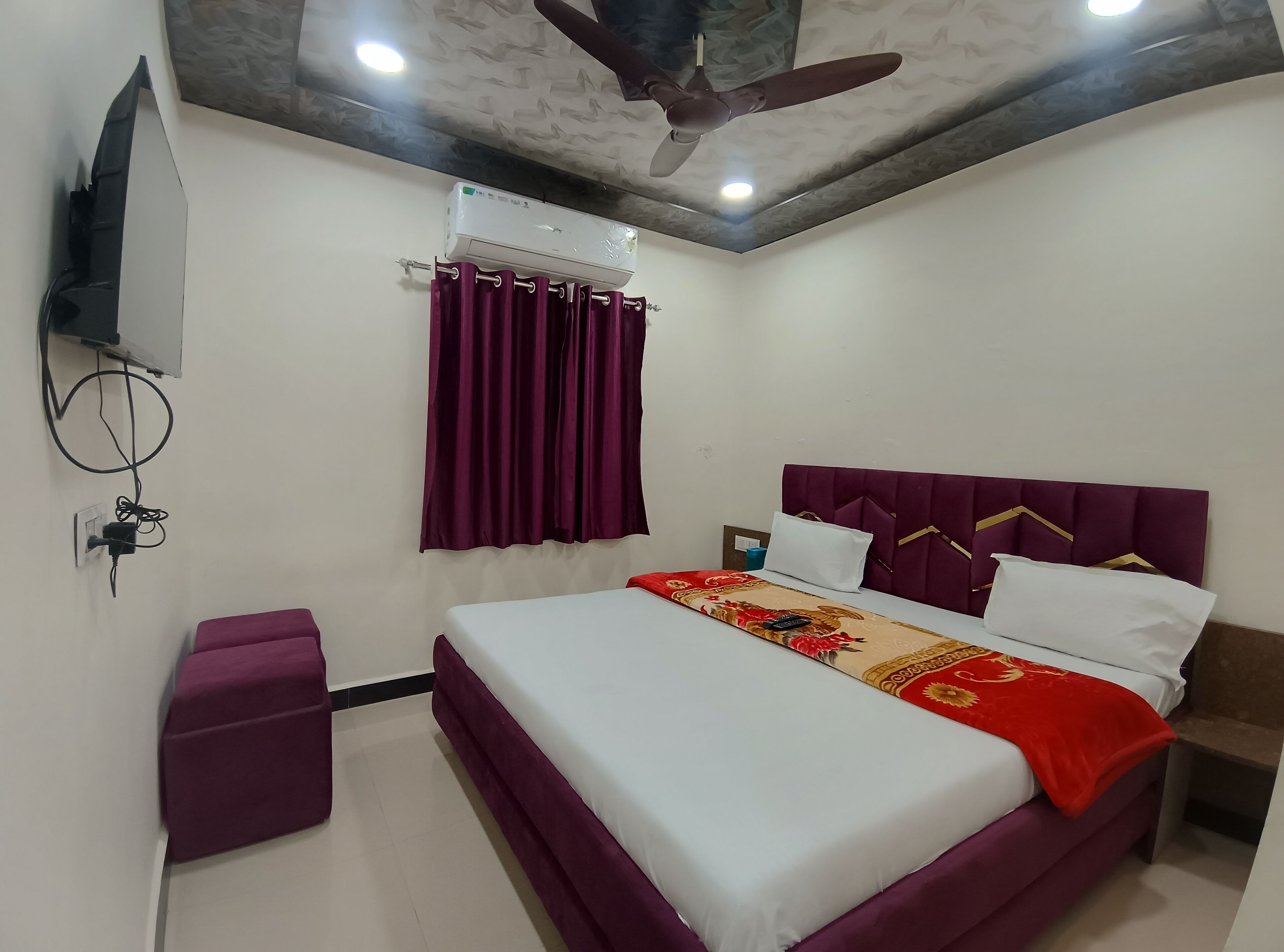 A bedroom with a bed, a ceiling fan, an air conditioning unit, and a TV mounted on the wall.