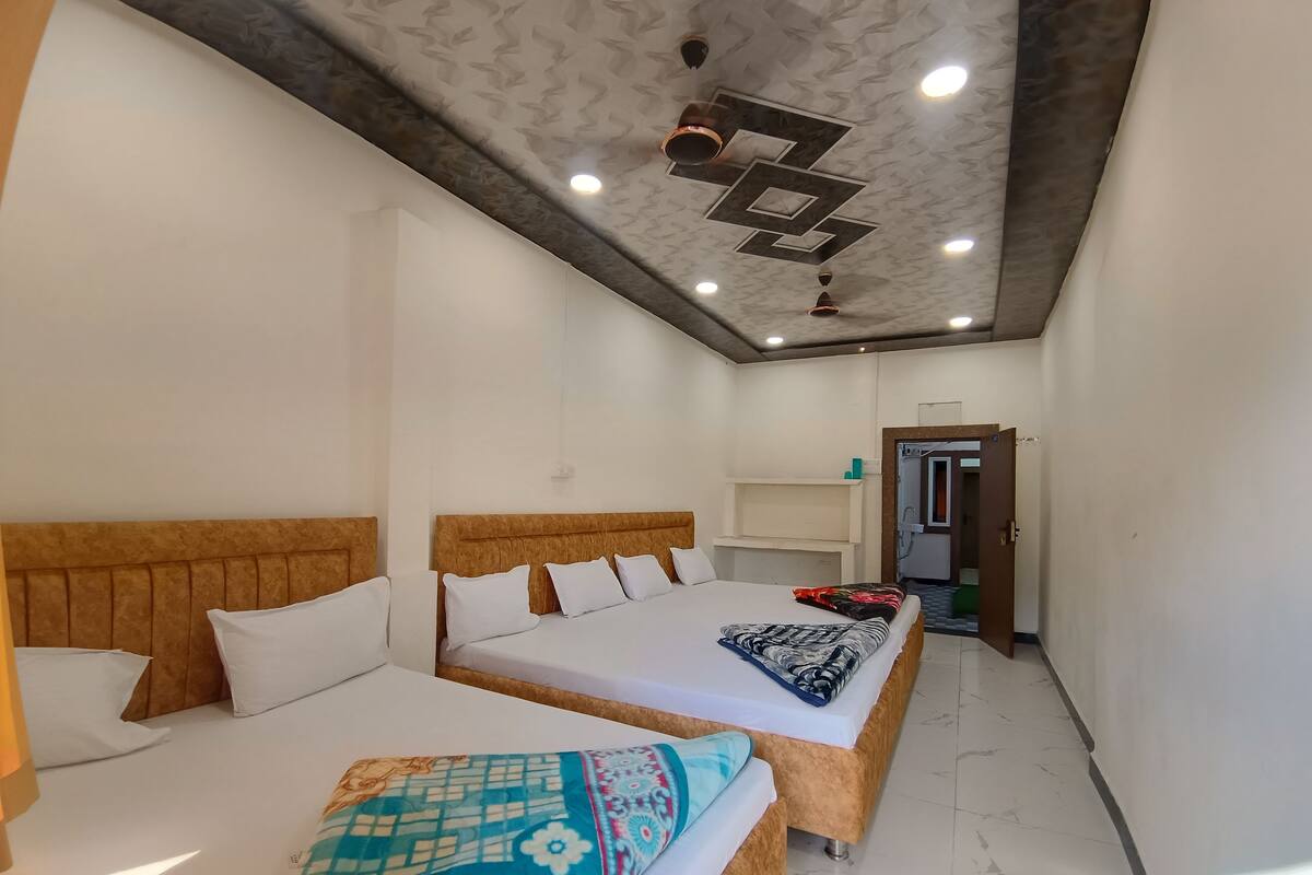 A hotel room with two beds, a wooden headboard, a ceiling with recessed lighting, and a door leading to a bathroom.