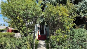 A pathway leading to a house with a red front door, surrounded by dense greenery and trees.