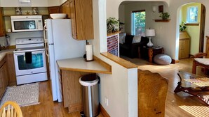 A compact kitchen with a microwave, oven, and refrigerator. There is a trash can and a wooden counter.
