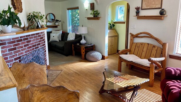 A cozy living room with a brick accent wall, wooden furniture, and a view into the kitchen.