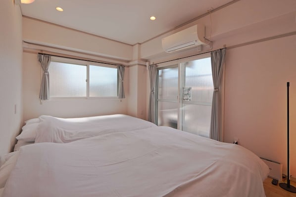 A hotel room with two beds, large windows, an air conditioning unit, and a standing lamp.