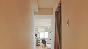 A narrow hallway with wooden flooring leading to a kitchen area with white cabinets and a dining table. - V.Close to Shinjuku Kabukicho E (Shinjuku-ku)