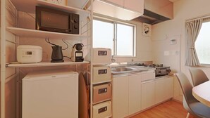A compact kitchenette with a microwave, toaster, kettle, and a stove. There is a small refrigerator, a sink, and a chair. - V.Close to Shinjuku Kabukicho E (Shinjuku-ku)